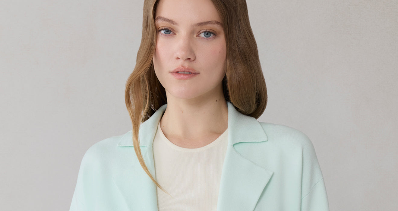 Woman wearing a light shirt cardigan over a white shirt on a plain background